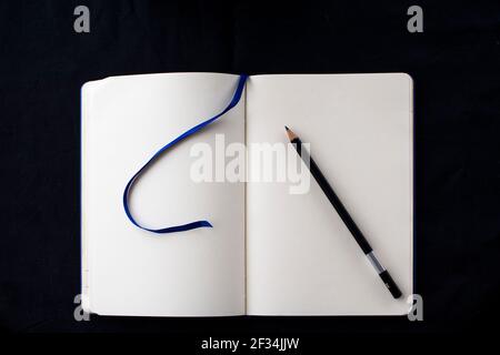 Öffnen Sie ein leeres Notizbuch mit einem Bleistift oben auf den Seiten auf schwarzem Hintergrund Stockfoto