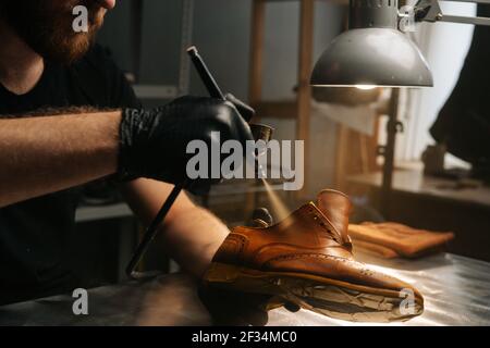 Nahaufnahme Hände von nicht erkennbaren Schuster tragen schwarze Handschuhe Sprühen Farbe von hellbraunen Lederschuhe. Stockfoto