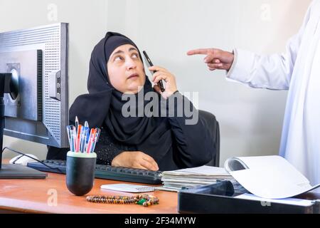 Arabisch-muslimische Angestellte, die von ihrem Chef wegen des Gesprächs beschimpft wurde Am Telefon bei der Arbeit Stockfoto