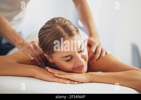 Professionelle Masseur tun therapeutische Massage. Frau genießt Massage in ihrem Haus. Junge Frau bekommen entspannende Körpermassage. Stockfoto