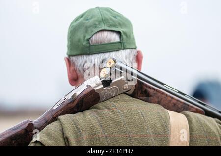 Ein älterer Mann mit weißen Haaren trägt eine Beretta-Pistole Auf seinen Schultern während eines Drehtages Stockfoto