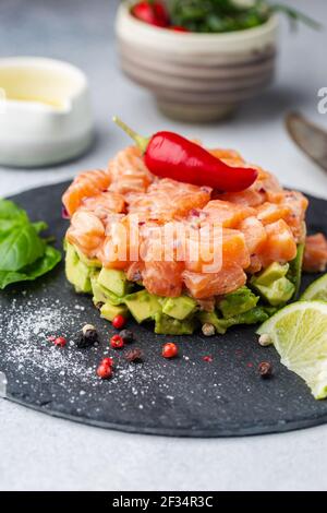 Köstliche avocado und roher Lachs Salat, Tartar, serviert auf einem schwarze Platte mit Kalk, hellen Hintergrund Stockfoto