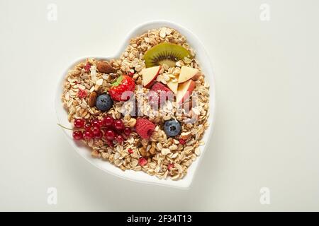 Draufsicht auf herzförmige Schale mit natürlichem Müsli und Frische Früchte auf grauem Hintergrund platziert Stockfoto