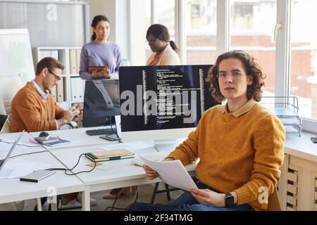 Porträt des jungen IT-Entwickler Blick auf Kamera, während posiert gegen Computer mit Code auf dem Bildschirm in Software-Produktionsstudio, Copy Space Stockfoto