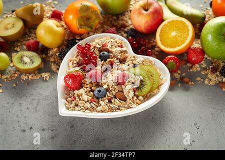 Von oben herzförmige Schale von Müsli auf grau platziert Tabelle neben verschiedenen Bio-Obst für ein gesundes Frühstück am Morgen Stockfoto