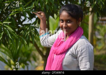 Nahaufnahme der indischen bengalischen Teenager-Mädchen trägt weiße Baumwolle Salwar mit rosa dhupatta zeigt grüne Mangoblätter in einem Garten, selektive Fokussierung Stockfoto