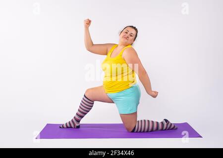 Eine dicke kaukasische Frau geht zum Sport. Abnehmen Übungen auf dem Teppich. Isolierter weißer Hintergrund im Studio. Stockfoto