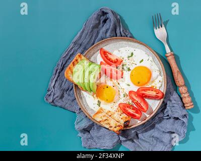 Zwei Spiegeleier mit Toast mit Avocado-Scheiben und Gemüse auf buntem Hintergrund. Frühstückskonzept. Gesundes vegetarisches Essen. Nahaufnahme, Kopierbereich Stockfoto