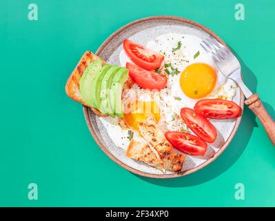 Zwei Spiegeleier mit Toast mit Avocado-Scheiben und Gemüse auf buntem Hintergrund. Frühstückskonzept. Gesundes vegetarisches Essen. Nahaufnahme, Kopierbereich Stockfoto