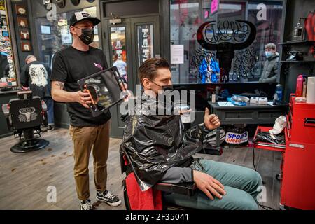 Barber Olly D'Urso schneidet die Haare von David Saunders, 38, aus Cardiff, bei Sleep When You're Dead Barbers in Duke St Arcade, Cardiff, während David nach seinem ersten Haarschnitt seit Sommer 2020 den Daumen nach oben zeigt. Friseure und Barbiere in Wales werden ab Montag zum ersten Mal im Jahr 2021 wiedereröffnet, da die Beschränkungen für Coronaviren gelockert werden, was die erste Aufhebung der Regeln für Dienstleistungen mit engen Kontakten seit der Sperre von Wales am 20. Dezember markiert. Geschäfte wie Nagelstudios und Schönheitssalons werden voraussichtlich bis mindestens April 12 geschlossen bleiben. Bilddatum: Montag, 15. März 2021. Stockfoto