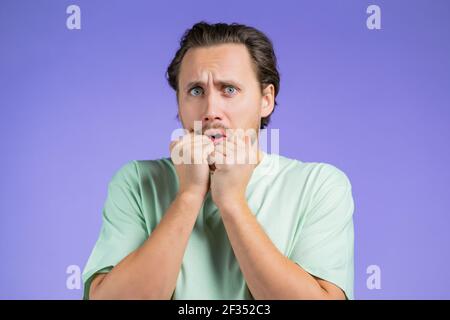 Erschrockener europäer hat Angst vor etwas und blickt mit großen Augen voller Schrecken über violettem Wandhintergrund in die Kamera. Stockfoto