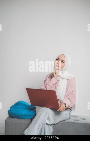asiatische muslimische Student hält Laptop und denken vor Weiß Stockfoto
