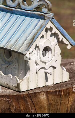 Aufwendig gebaute weiße Vogelhaus mit hellblauem Dach und gedeckelt Verzierte Besatz zeigt zwei Öffnungen mit Sitzstangen auf einem Brauner Baumstumpf Stockfoto