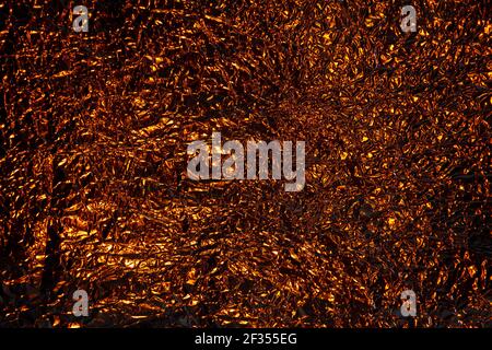 Abstrakt golden oder Kupfer Aluminium zerknittert Folie Hintergrund Textur reflektierend Dunkles goldenes Licht Stockfoto