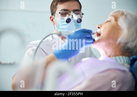 Zahnarzt in Zahnscheinwerfer Lupen Behandlung von alten Frau Zähne Stockfoto