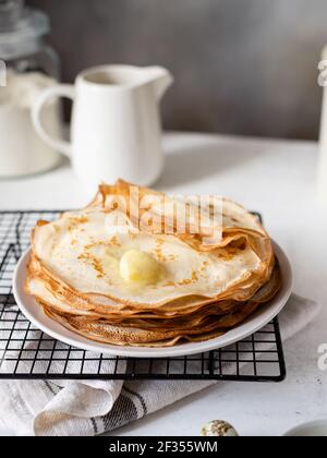 Blini oder Crepe oder dünne Pfannkuchen Stapel auf Tisch mit Butter gekrönt. Selektiver Fokus. Vertikales Bild. Grauer Hintergrund Stockfoto