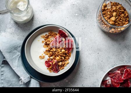 Schüssel mit Naturjoghurt, Müsli und blutigem Orange auf grauem Betongrund. Sauber essen. Horizontales Bild, Kopierer Platz, flach legen. Stockfoto