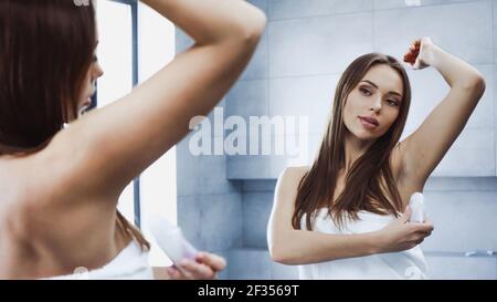 Junge Frau mit erhobener Hand Deodorant Rolle auf in Badezimmer Stockfoto