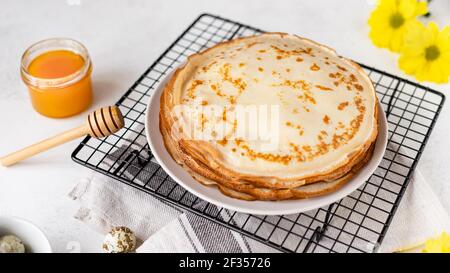 Traditionelle hausgemachte dünne Pfannkuchen, Blini mit Honig auf weißem Hintergrund mit Frühlingsblumen. Russische Maslenitsa. Horizontales Bild, Seitenansicht Stockfoto