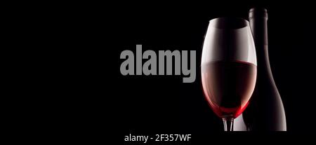 Ein Glas und eine Flasche Rotwein auf schwarzem Hintergrund. Panoramafoto, Kopierraum. Stockfoto