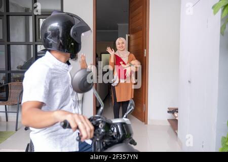 Mann, der mit dem Motorrad zum Büro fährt und Auf Wiedersehen zuwinkt Seine Frau Stockfoto