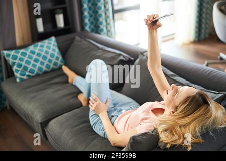 Charmante Frau liegt auf der Couch und macht Selfie zu Hause Stockfoto