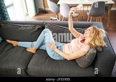 Fröhliche Frau liegt auf der Couch und macht Selfie zu Hause Stockfoto