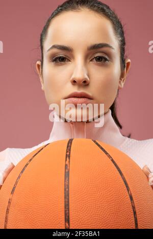 Attraktive junge Frau mit Basketball-Ball posiert im Studio Stockfoto