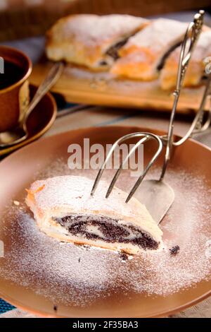 Eine elegante Gabel hält eine Mohnrolle vor dem Hintergrund einer Tasse Kaffee. Stockfoto