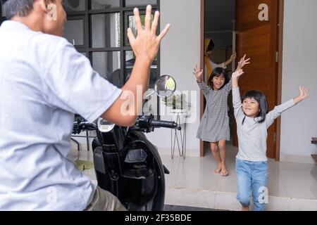 muslimischer asiatischer Vater, der von der Arbeit nach Hause zurückkehrt, ist willkommen Von seiner Familie an einer Haustür Stockfoto