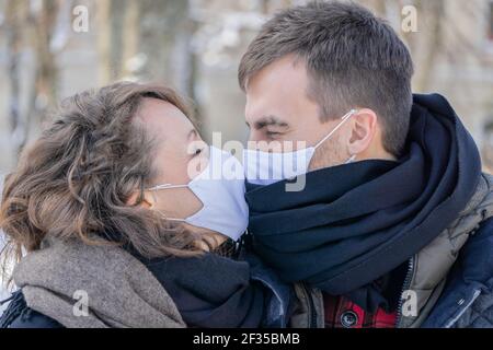 Paar küssen tragen Gesichtsmasken im Freien. Mann und Frau küssen durch Gesichtsmasken im Freien. Schönes Paar in schützenden medizinischen Masken Blick auf jeden Stockfoto