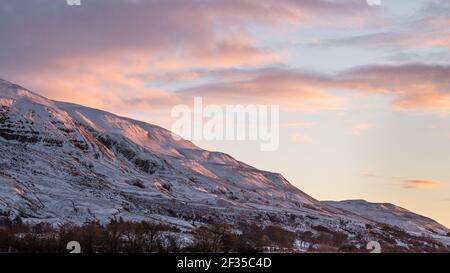 Ein frühes Morgenglühen auf den Winterhügeln, wenn die Sonne auf den Campsie Fells hinter Lennoxtown, Schottland, aufgeht Stockfoto