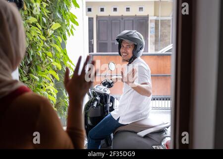 asiatischer Ehemann winkt Auf Wiedersehen zu seiner Frau vor dem Verlassen aus Mit dem Motorrad Stockfoto