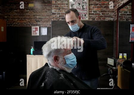 Lissabon, Portugal. März 2021, 15th. Ein Barbier mit Gesichtsmaske schneidet am 15. März 2021 die Haare eines Kunden in einem Friseurladen in Oeiras, Portugal. Die portugiesische Regierung hat einen vierstufigen Plan zur Lockerung der COVID-19-Beschränkungen im Laufe des Impfprogramms aufgestellt, wobei die erste Stufe am 15. März mit der Wiedereröffnung von Kindergärten, Kindergärten und Grundschulen sowie Friseuren, Barbierläden und Buchhandlungen beginnt. Quelle: Pedro Fiuza/ZUMA Wire/Alamy Live News Stockfoto