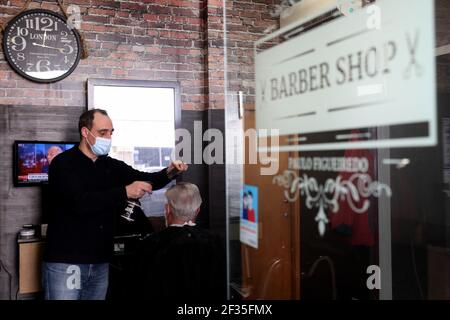 Lissabon, Portugal. März 2021, 15th. Ein Barbier mit Gesichtsmaske schneidet am 15. März 2021 die Haare eines Kunden in einem Friseurladen in Oeiras, Portugal. Die portugiesische Regierung hat einen vierstufigen Plan zur Lockerung der COVID-19-Beschränkungen im Laufe des Impfprogramms aufgestellt, wobei die erste Stufe am 15. März mit der Wiedereröffnung von Kindergärten, Kindergärten und Grundschulen sowie Friseuren, Barbierläden und Buchhandlungen beginnt. Quelle: Pedro Fiuza/ZUMA Wire/Alamy Live News Stockfoto