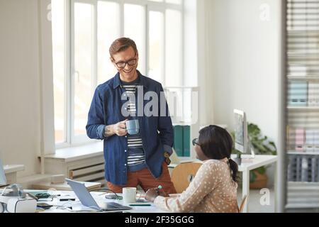 Porträt eines lächelnden Mannes, der mit einem afroamerikanischen Kollegen spricht, während er eine Kaffeepause im modernen weißen Büro genießt, Kopierraum Stockfoto