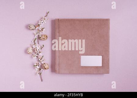 Flach legen mit einem rosa Fotoalbum oder Buch mit einem Metallrahmen für die Inschrift, Frühlingszweige mit Blumen und Ostereier auf einem rosa Hintergrund. Bis Stockfoto