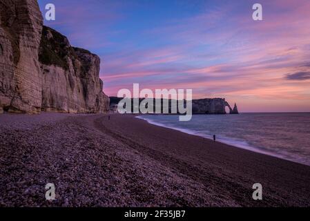 Lange und steile Klippen enden am natürlichen Steinbogen Porte d'Aval und der Felsennadel Aiguille. Zwielichtiger rosafarbener Himmel über der Meeresküste. Stockfoto