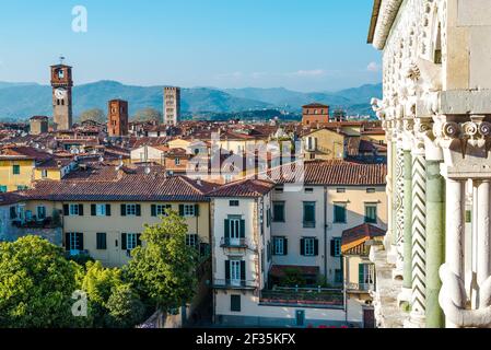 Blick über die Dächer der historischen Stadt Lucca, Italien. Mehrere hohe Türme ragen darüber. Berge im Hintergrund. Stockfoto