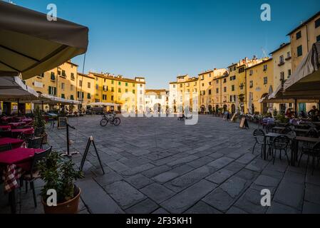 Tag auf dem berühmten Platz Piazza dell'Anfiteatro, Lucca, Italien. Menschen, die an den Tischen des Cafés und des Restaurants des Platzes herumlaufen und sitzen. Stockfoto