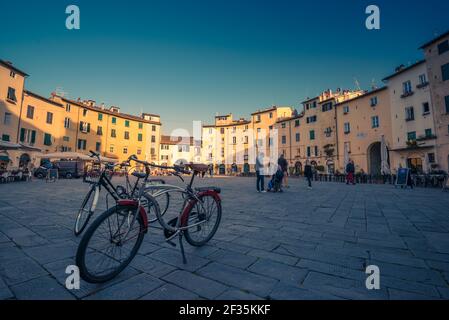 Weitwinkelansicht von zwei Fahrrädern, die auf dem Platz Piazza dell'Anfiteatro, Lucca, Italien, stehen. Menschen genießen den Tag im historischen Teil der Stadt. Stockfoto