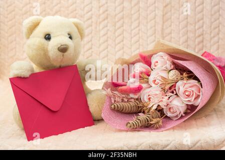 Stofftier Spielzeug Polar Teddybär mit Blumen und roten Umschlag mit Herzlichen Glückwunsch. Das Konzept eines Kinderurlaubs, eines Müttertages, eines Geburtstags Stockfoto