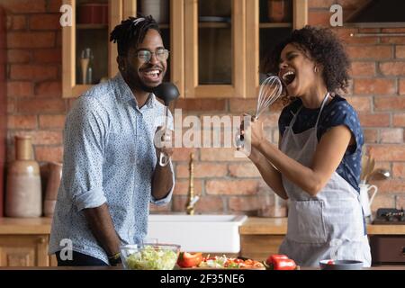 Junge afrikanische Paar singen Lied in Mikrofonen von Küchenutensilien Stockfoto