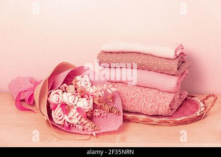 Stapel von gefalteten Wollgestrickpulvern oder Pullovern in rosa Pastellfarben auf Tisch mit Blume. Nahaufnahme von warmen gemütlichen bequemen monochromen Kleidung fo Stockfoto