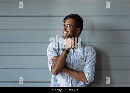 Lächelnder, tausendjähriger afrikanischer Mann, der vor einer grauen Wand posiert, schaut weg Stockfoto