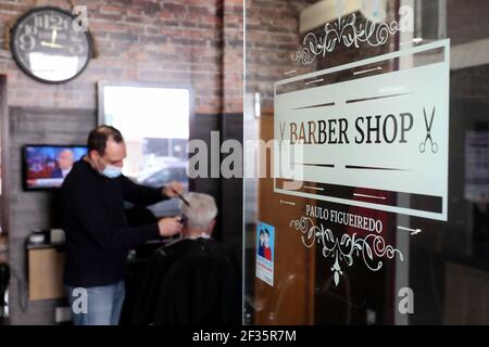 Lissabon, Portugal. März 2021, 15th. Ein Barbier mit Gesichtsmaske schneidet die Haare eines Kunden in einem Friseurladen in Oeiras, Portugal, 15. März 2021. Ab März 15, Bildungseinrichtungen für die frühe Kindheit, Take-away-Shops, Beauty-Studios, Buchhandlungen, Autohandel, Und die Immobilienvermittlung in Portugal kann nach mehr als zwei Monaten der Sperre eröffnet werden, um die COVID-19-Pandemie einzudämmen. Quelle: Pedro Fiuza/Xinhua/Alamy Live News Stockfoto