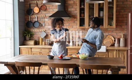 Fröhliche Millennial schwarz paar haben Spaß an der Küche singen laut Stockfoto