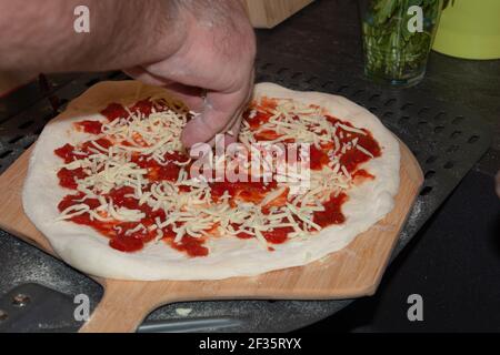 Frisch zubereitete Margherita Pizza auf Holzsteppich vor dem Backen mit Mann Hand Stockfoto