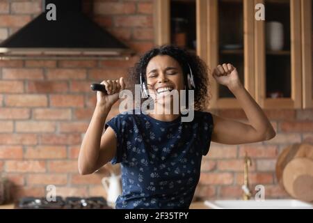 Aktive afrikanische Frau im Headset singen in der Küche halten Schneebesen Stockfoto