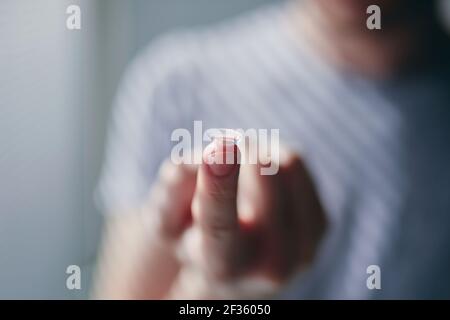 Nahaufnahme der Kontaktlinse am Finger eines jungen Mannes bei Morgenlicht. Themen Sehvermögen, Sehfehler und tägliche Routine. Stockfoto
